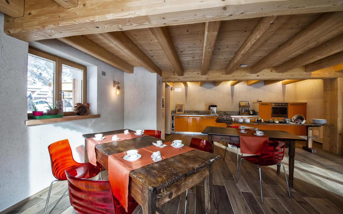 Sala da pranzo rustica con tavoli in legno, sedie rosse e cucina moderna.