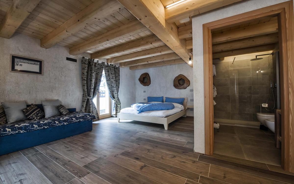 Camera accogliente con letto, divano, bagno privato e travi in legno a vista.