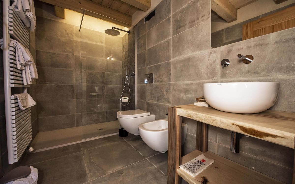 Bagno moderno con doccia a pioggia, lavabo su piano in legno e sanitari sospesi.