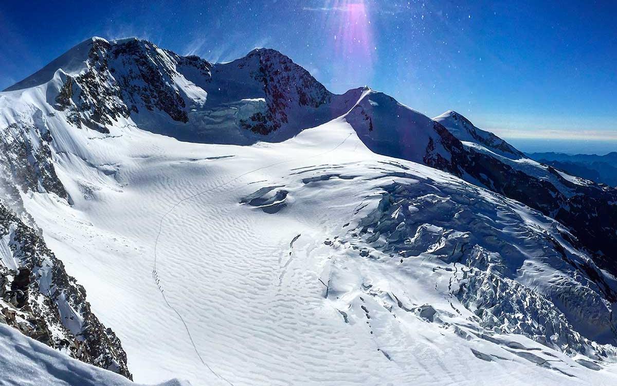 Panorama montano innevato con cielo limpido e sole splendente.