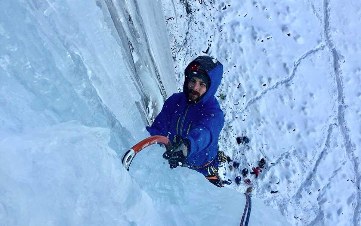 Alpinista scala una parete di ghiaccio in un paesaggio innevato.