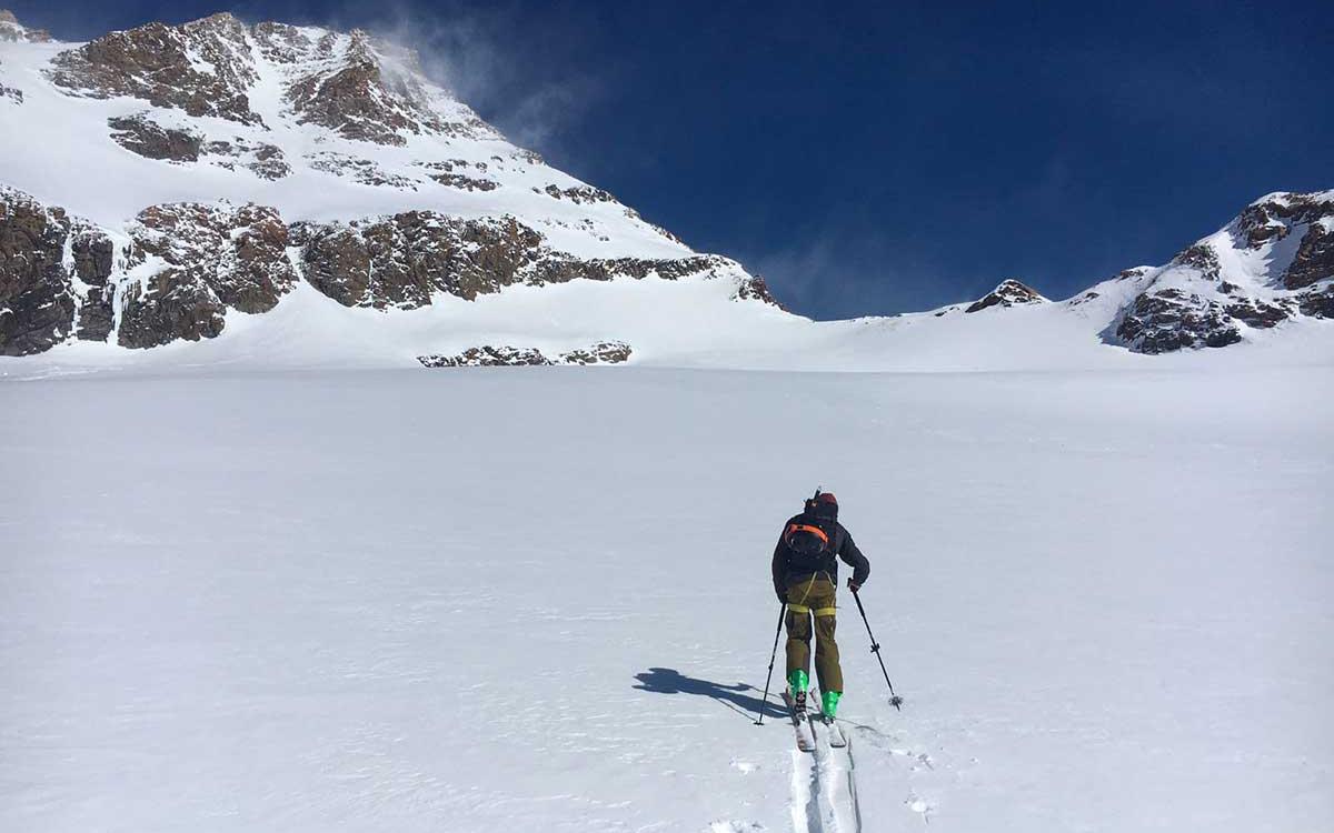 Scialpinista che risale una montagna innevata sotto un cielo limpido.