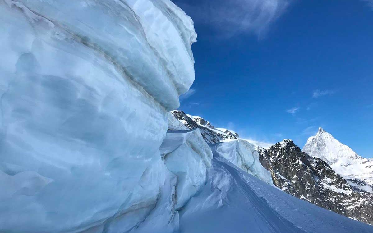 Ghiacciaio con montagne innevate sullo sfondo e cielo azzurro limpido.