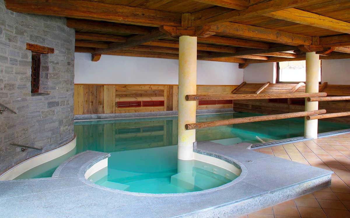 Piscina interna con colonne e struttura in legno, ambiente caldo e rilassante.