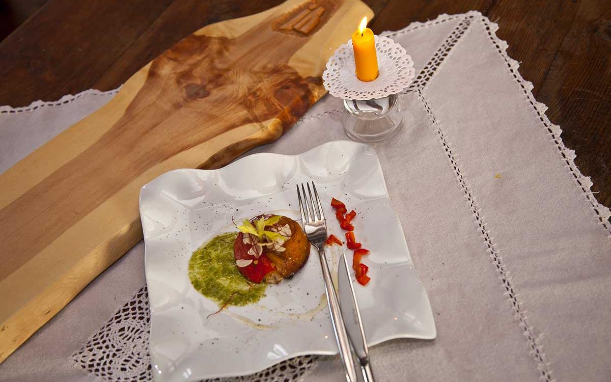 Piatto gourmet con salsa verde, candela accesa e tovaglietta ricamata.