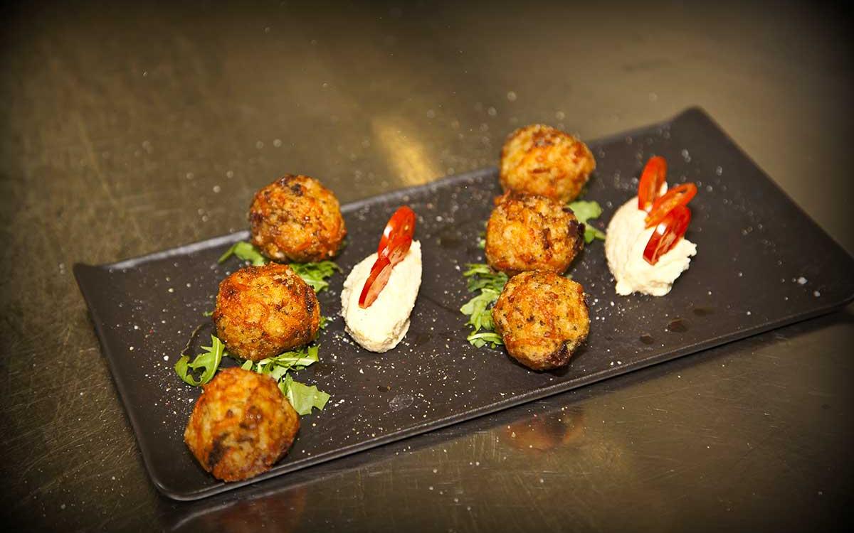 Polpette fritte servite con crema e guarnite con peperoncini rossi su un piatto nero.