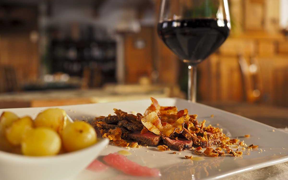 Piatto di carne con patate e bicchiere di vino rosso in un ristorante.