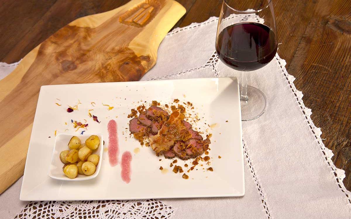 Tagliata di carne con contorno di patate e bicchiere di vino rosso.