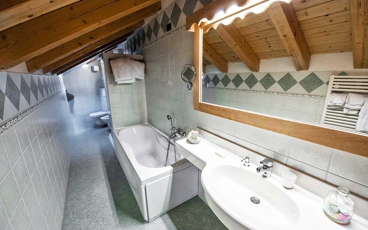 Bagno mansardato con vasca, lavabo, specchio grande, e soffitto in legno.