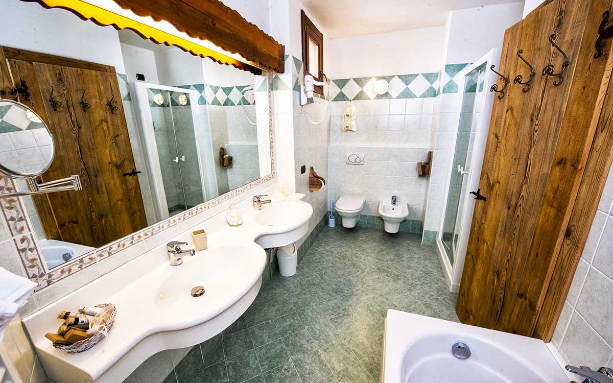 Bagno spazioso con doppio lavabo, doccia, bidet, e dettagli in legno rustico.