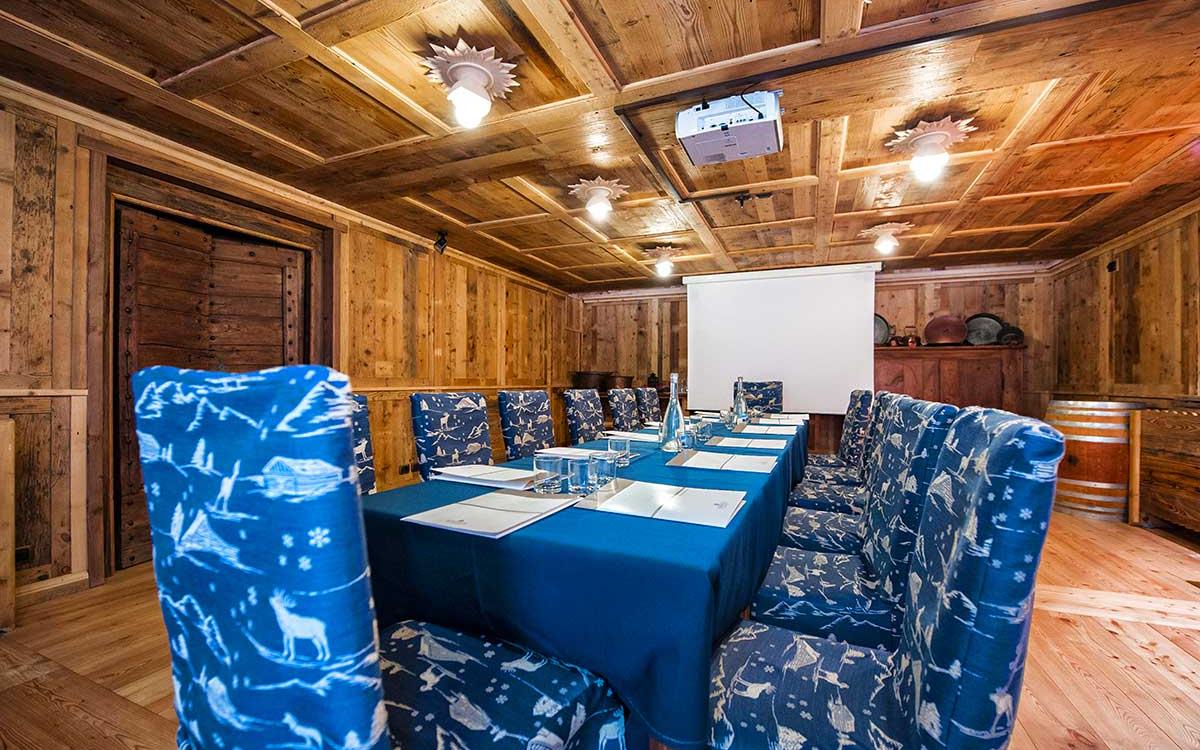 Sala riunioni rustica in legno con sedie blu e proiettore.