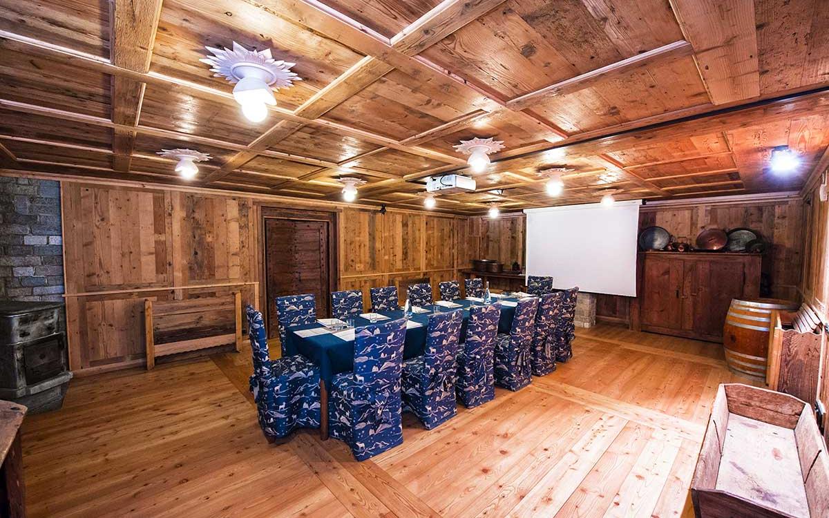 Sala rustica in legno con proiettore, tavolo e sedie coperte da tessuto decorato.