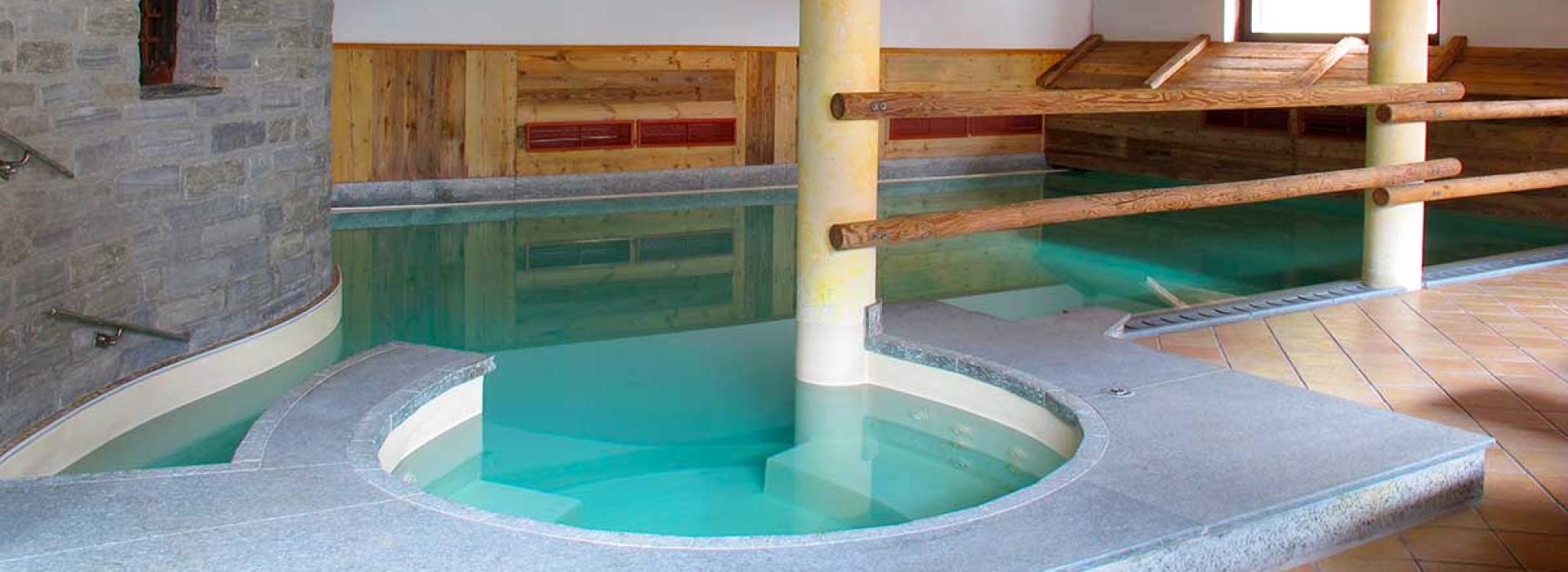 Piscina interna con colonne e struttura in legno, ambiente caldo e rilassante.