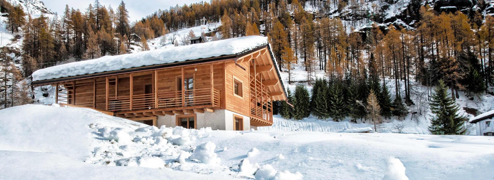 Chalet di legno in montagna con neve e alberi innevati sullo sfondo.