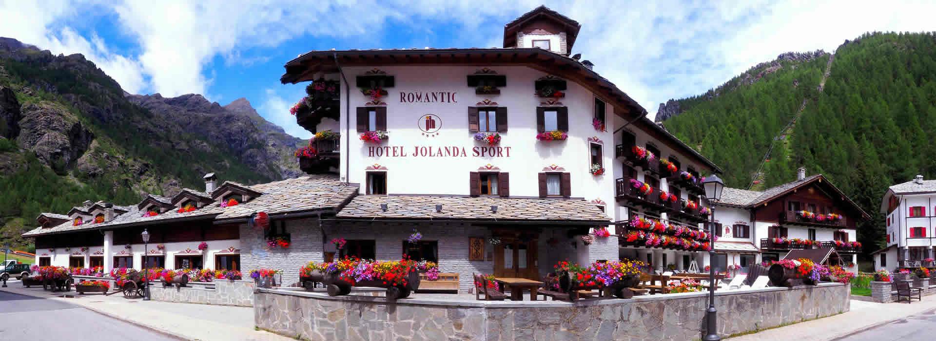 Hotel Jolanda Sport: struttura romantica con fiori, immersa tra montagne verdi.