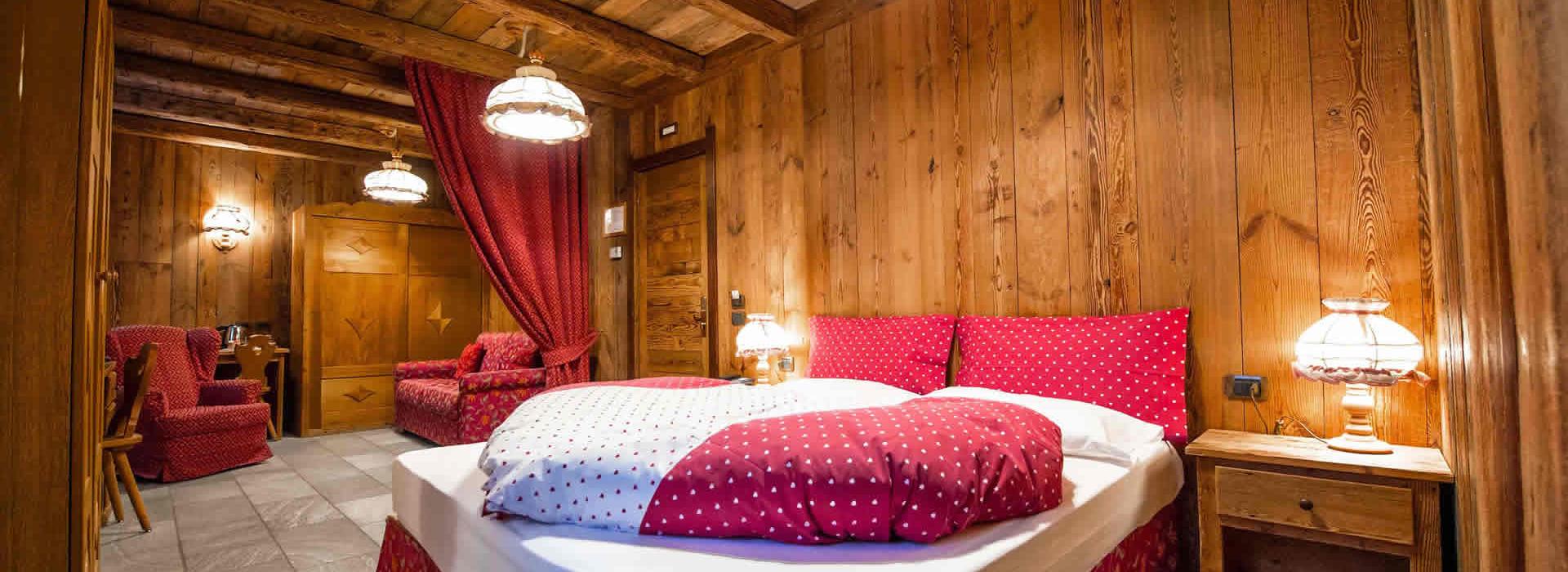 Camera rustica con letto matrimoniale, rivestimenti in legno, e arredamento rosso a pois.