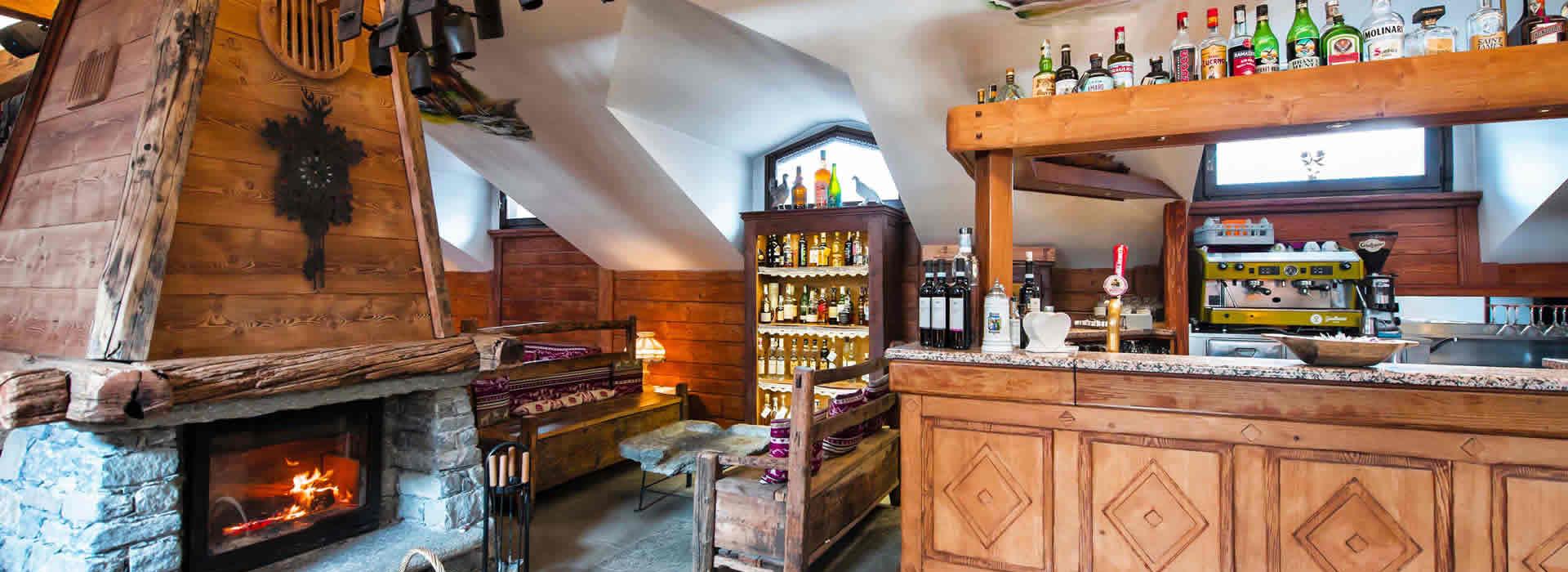 Accogliente bar in stile rustico con camino, legno e bottiglie di liquori esposte.