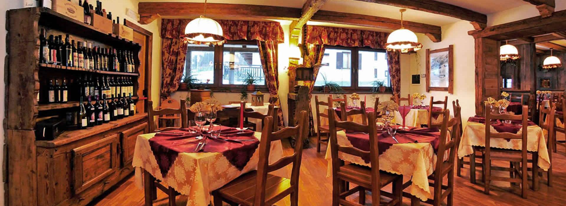 Ristorante rustico con travi in legno, tavoli apparecchiati e scaffali pieni di bottiglie di vino.