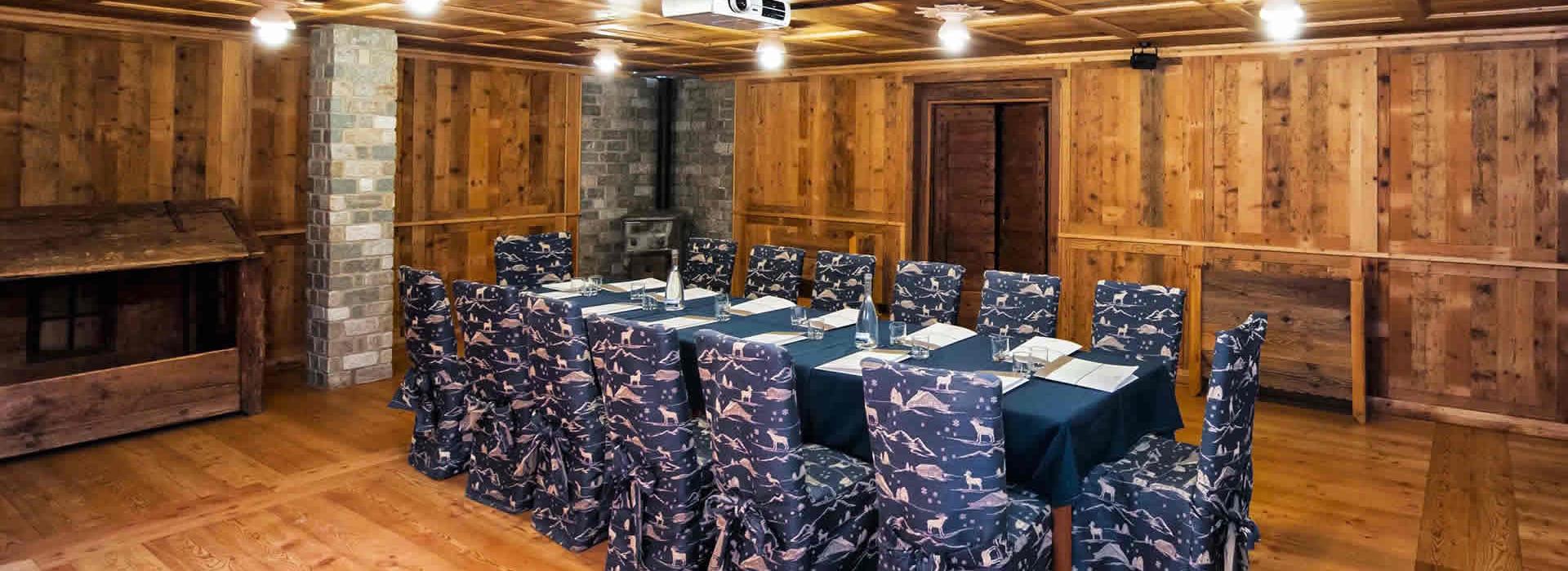 Sala riunioni rustica con pareti in legno e sedie rivestite.