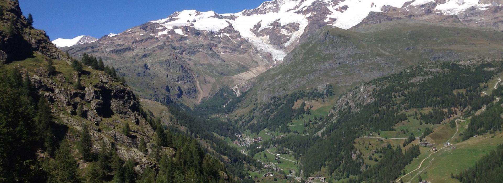 Panorama montano con cime innevate, vallate verdi e villaggi alpini sotto un cielo limpido.