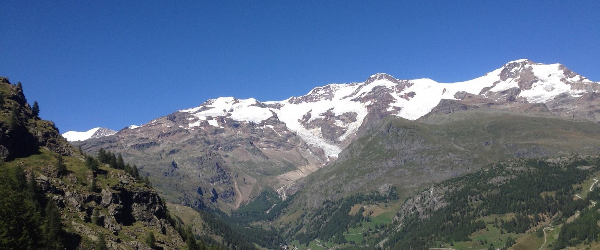 Panorama alpino con montagne innevate, cielo azzurro e vallate verdi.