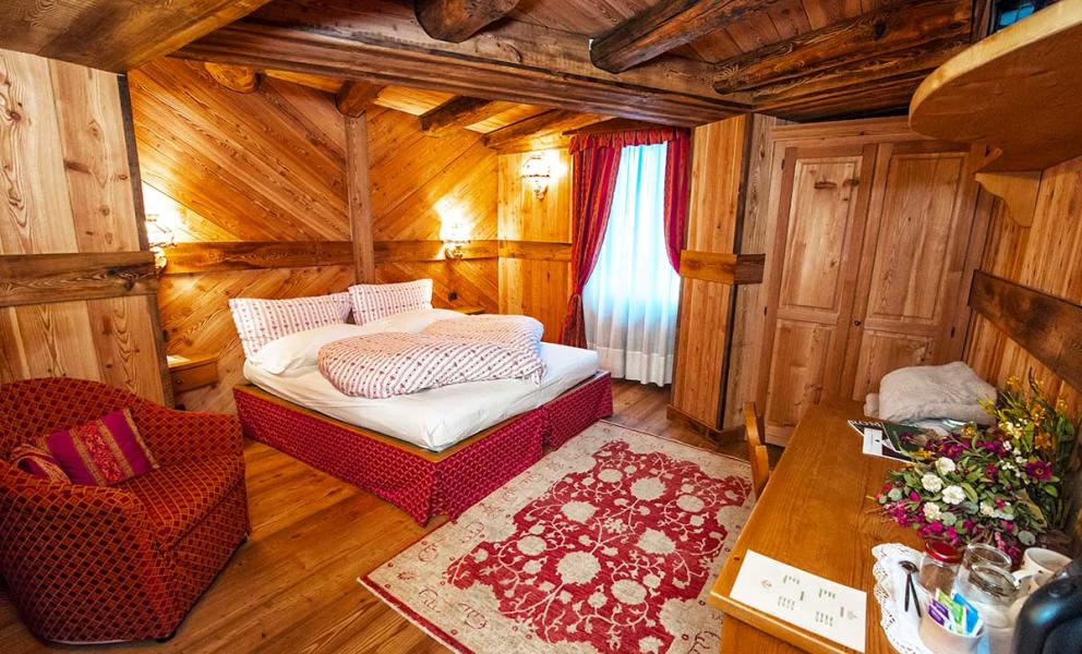 Camera accogliente in legno con letto matrimoniale, poltrona e tappeto rosso decorato.