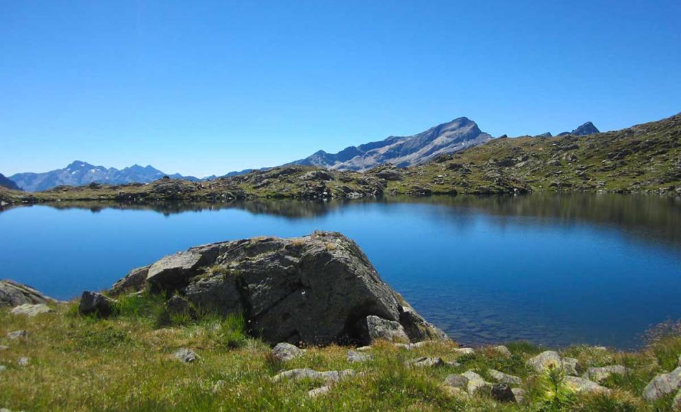 Lago di montagna con acque cristalline, circondato da prati e montagne.